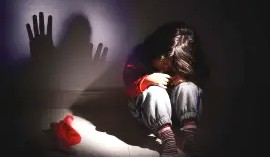 Young girl sitting alone in fear with a shadowed hand on the wall